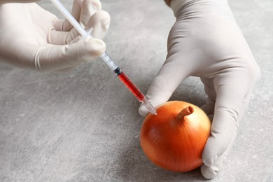 Photo of GMO concept. Scientist injecting something into onion at grey table, closeup