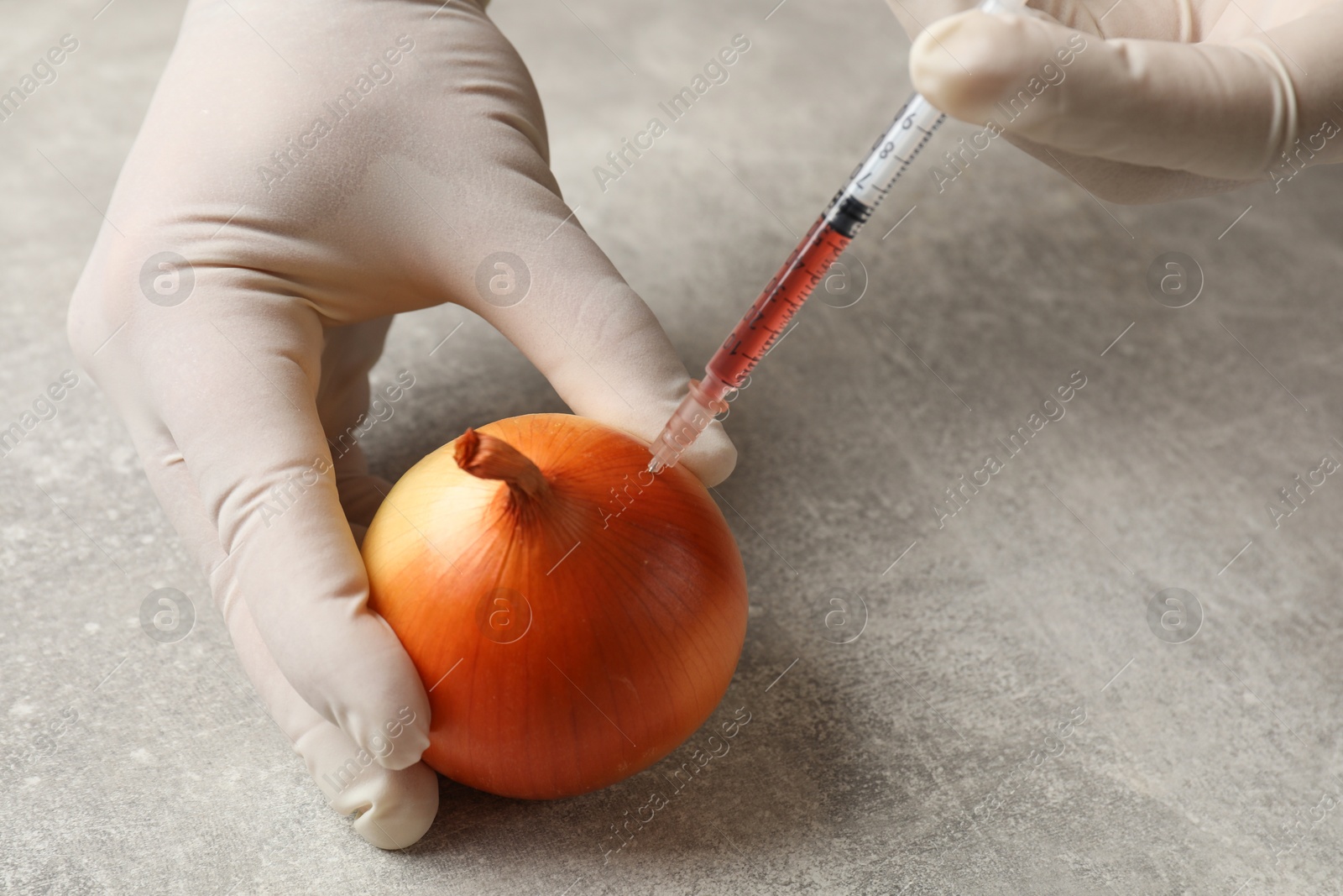 Photo of GMO concept. Scientist injecting something into onion at grey table, closeup