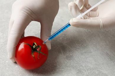 Photo of GMO concept. Scientist injecting something into fresh tomato at grey table, closeup