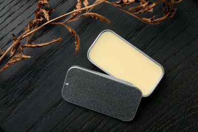 Photo of Natural solid perfume and dry branch on black wooden table, flat lay