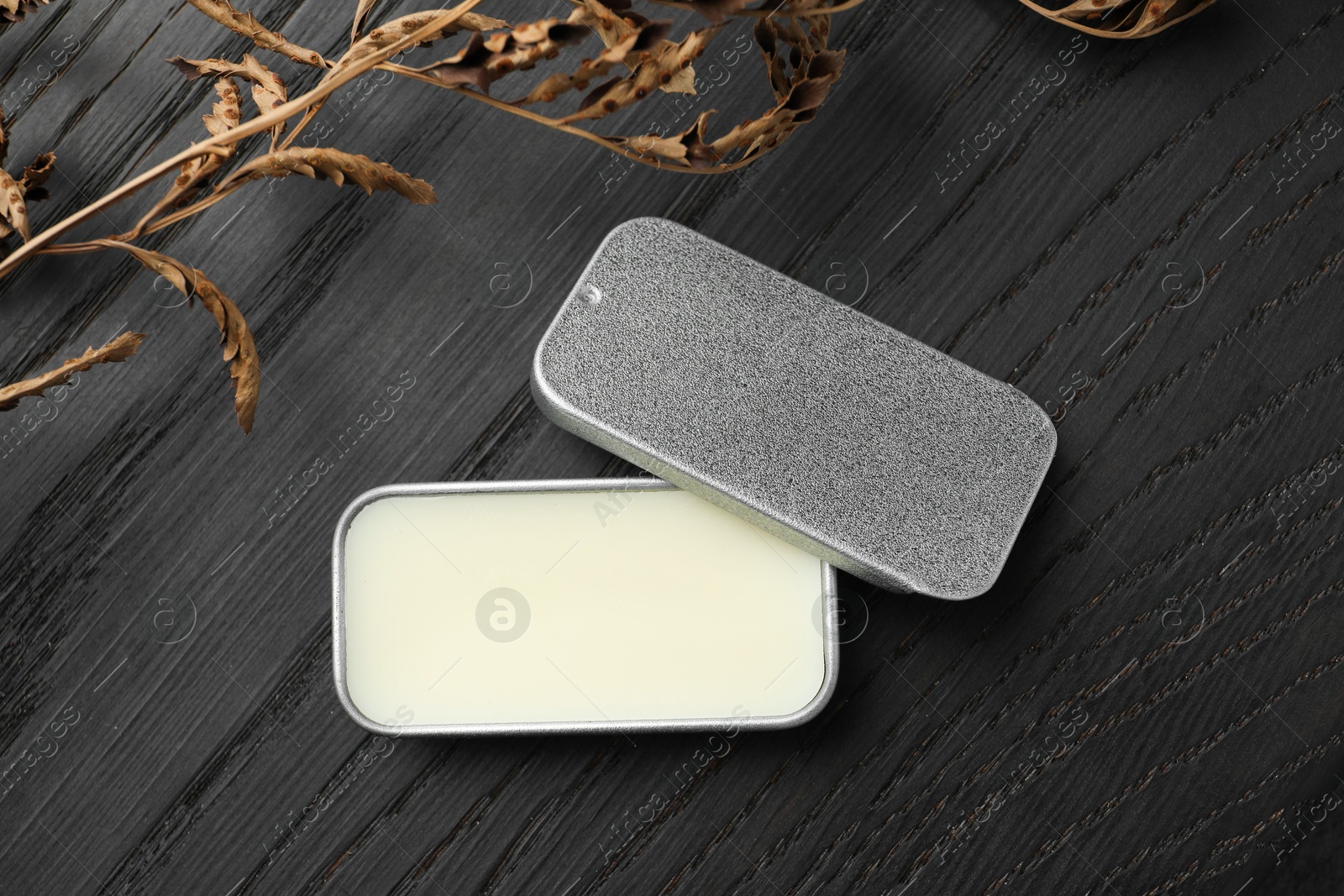 Photo of Natural solid perfume and dry branch on black wooden table, flat lay