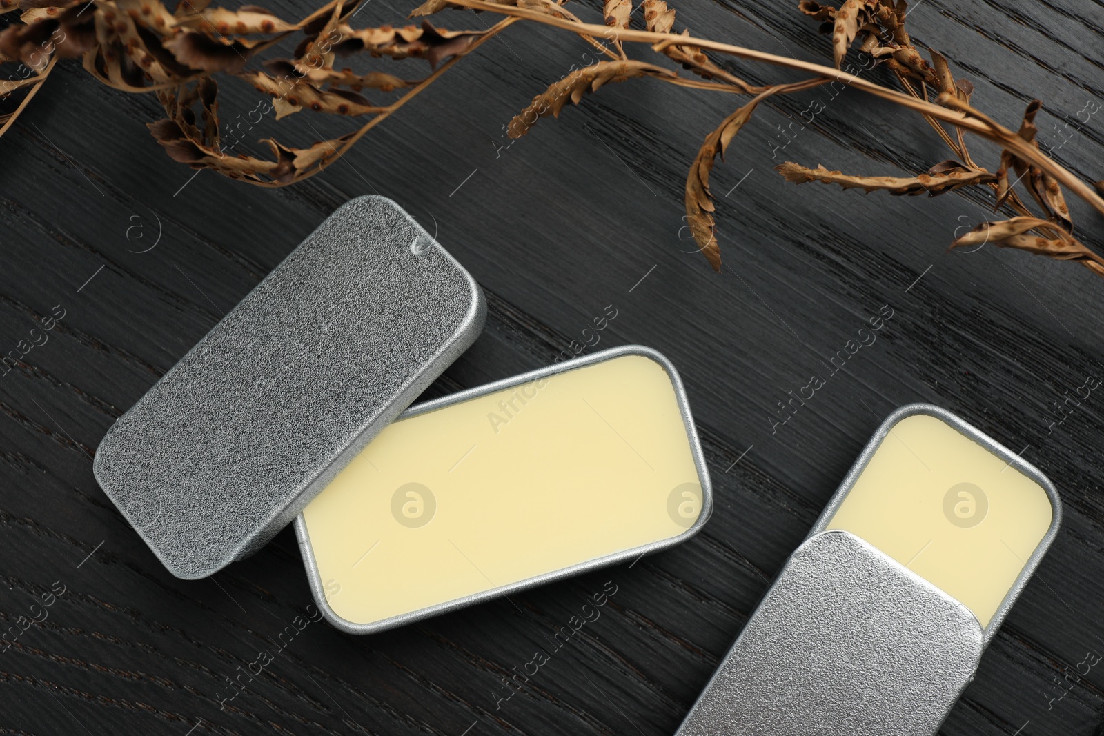 Photo of Natural solid perfume and dry branch on black wooden table, flat lay