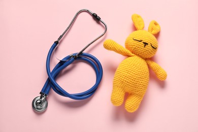 Photo of Pediatrics concept. Toy bunny with stethoscope on pink background, top view