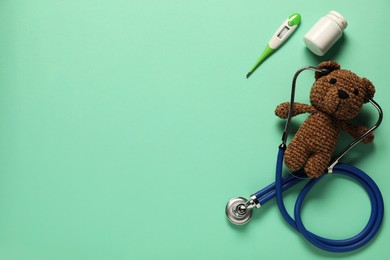 Photo of Pediatrics concept. Toy bear with stethoscope, pills and thermometer on turquoise background, flat lay. Space for text