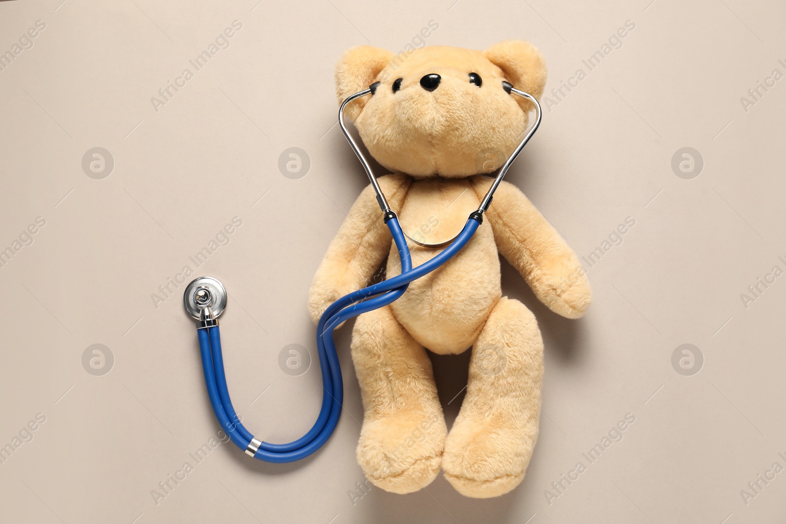 Photo of Pediatrics concept. Teddy bear with stethoscope on beige background, top view