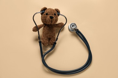 Photo of Pediatrics concept. Toy bear with stethoscope on beige background, top view