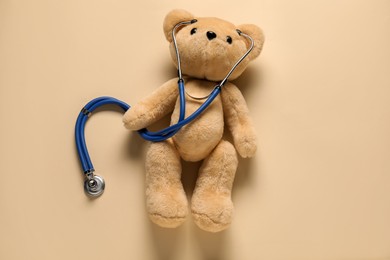 Photo of Pediatrics concept. Teddy bear with stethoscope on beige background, top view