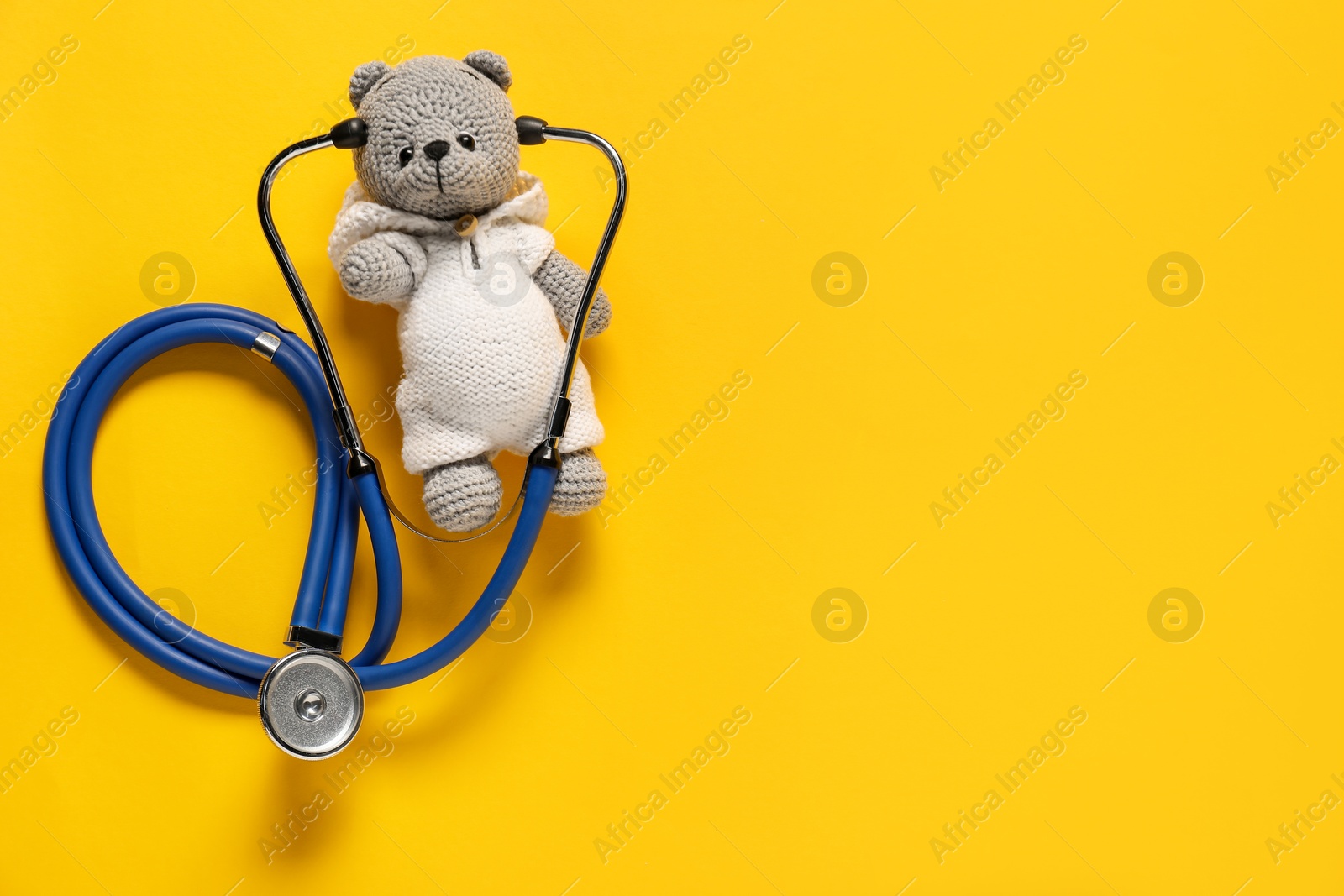 Photo of Pediatrics concept. Toy bear with stethoscope on yellow background, top view. Space for text