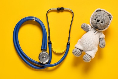 Photo of Pediatrics concept. Toy bear with stethoscope on yellow background, top view