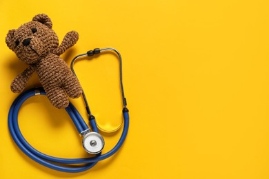 Photo of Pediatrics concept. Toy bear with stethoscope on yellow background, top view. Space for text