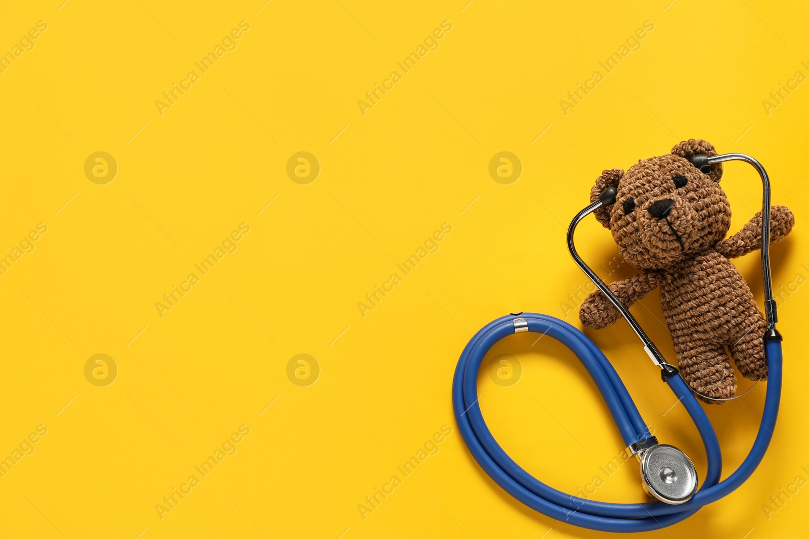 Photo of Pediatrics concept. Toy bear with stethoscope on yellow background, top view. Space for text