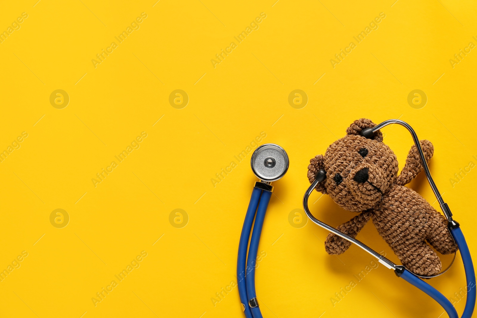 Photo of Pediatrics concept. Toy bear with stethoscope on yellow background, top view. Space for text