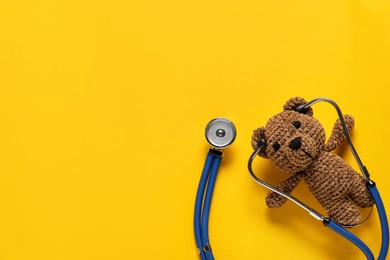 Photo of Pediatrics concept. Toy bear with stethoscope on yellow background, top view. Space for text