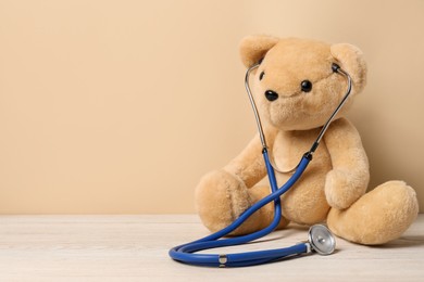 Photo of Pediatrics concept. Teddy bear with stethoscope on wooden table against beige background, space for text