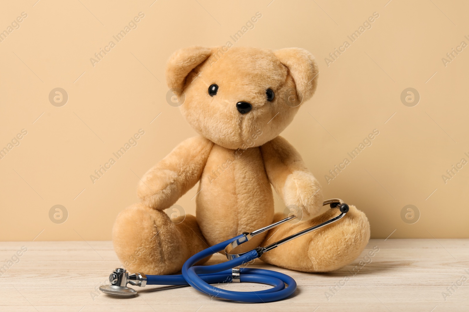 Photo of Pediatrics concept. Teddy bear with stethoscope on wooden table against beige background