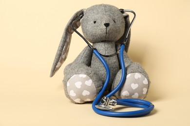 Photo of Pediatrics concept. Toy bunny with stethoscope on beige background