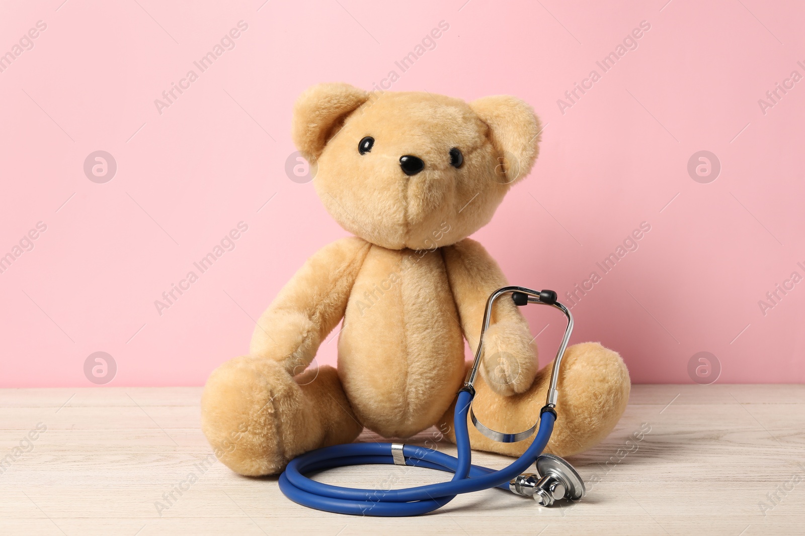 Photo of Pediatrics concept. Teddy bear with stethoscope on wooden table against pink background