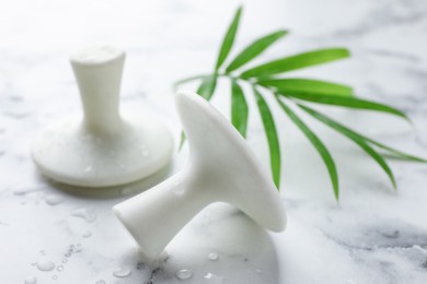 Photo of Wet spa stones and green palm leaf on white marble table, closeup