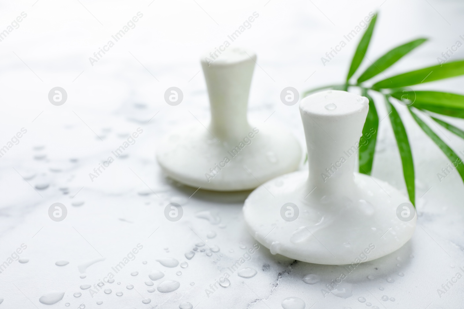 Photo of Wet spa stones and green palm leaf on white marble table, closeup. Space for text