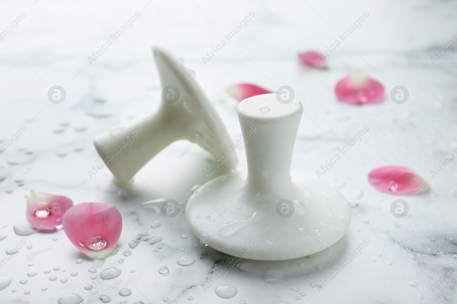 Photo of Wet spa stones and petals on white marble table, closeup