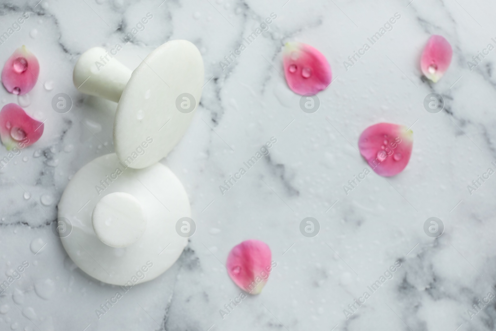 Photo of Wet spa stones and petals on white marble table, flat lay