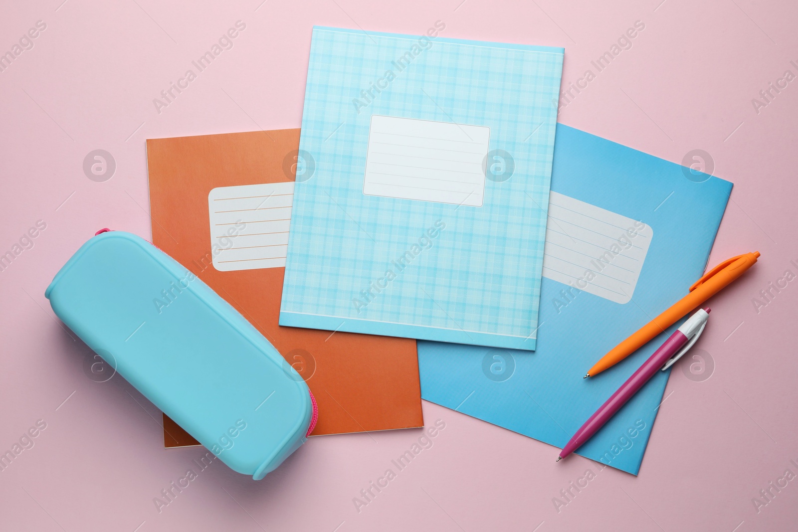 Photo of Copybooks, pens and pencil case on pink background, flat lay