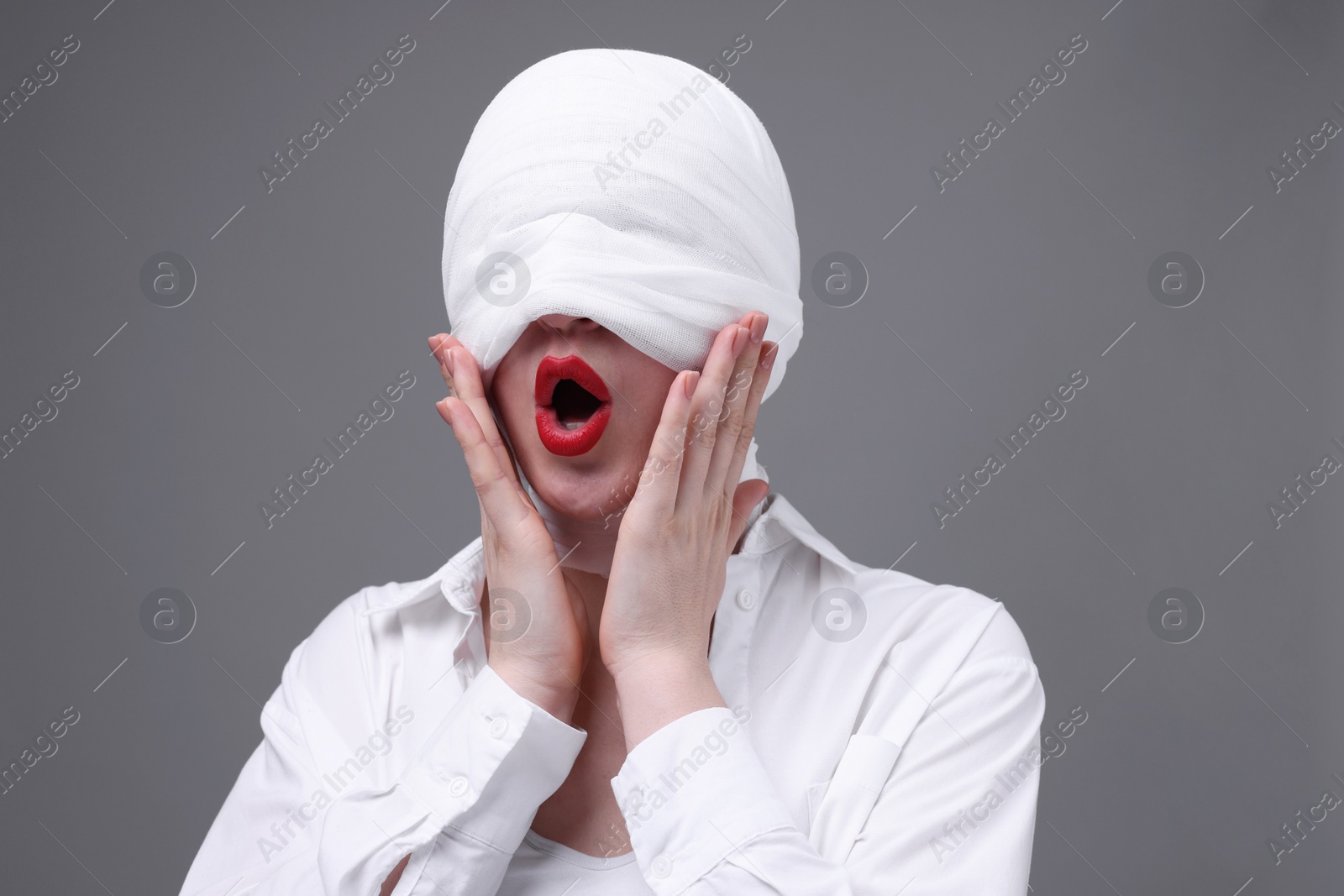 Photo of Woman with face wrapped in medical bandage after plastic surgery operation on grey background