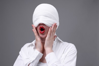 Woman with face wrapped in medical bandage after plastic surgery operation on grey background