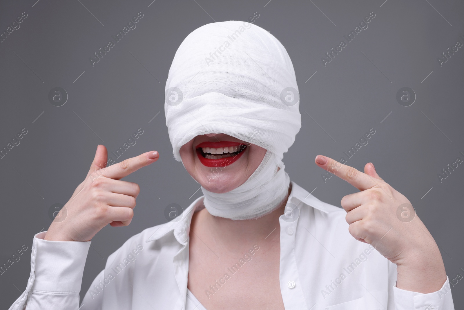 Photo of Woman with face wrapped in medical bandage after plastic surgery operation on grey background