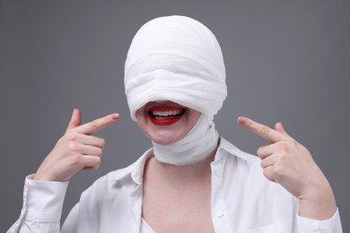 Photo of Woman with face wrapped in medical bandage after plastic surgery operation on grey background