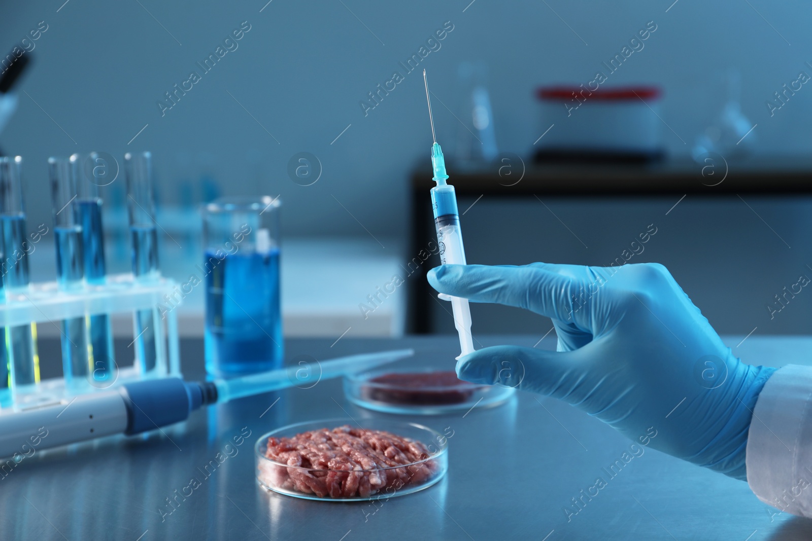 Photo of GMO concept. Scientist with syringe and minced meat on table in laboratory, closeup