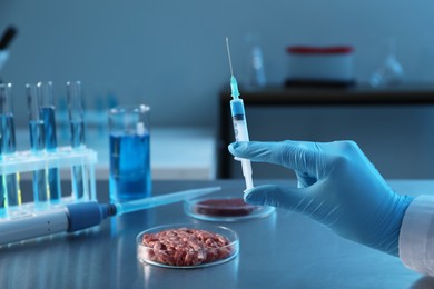 Photo of GMO concept. Scientist with syringe and minced meat on table in laboratory, closeup