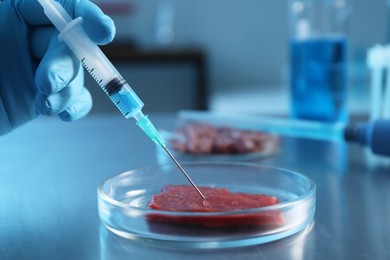 Photo of GMO concept. Scientist injecting something into piece of meat at table in laboratory, closeup