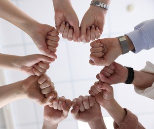 Photo of Unity concept. People holding fists together indoors, bottom view