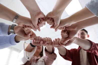 Photo of Unity concept. People holding fists together indoors, low angle view