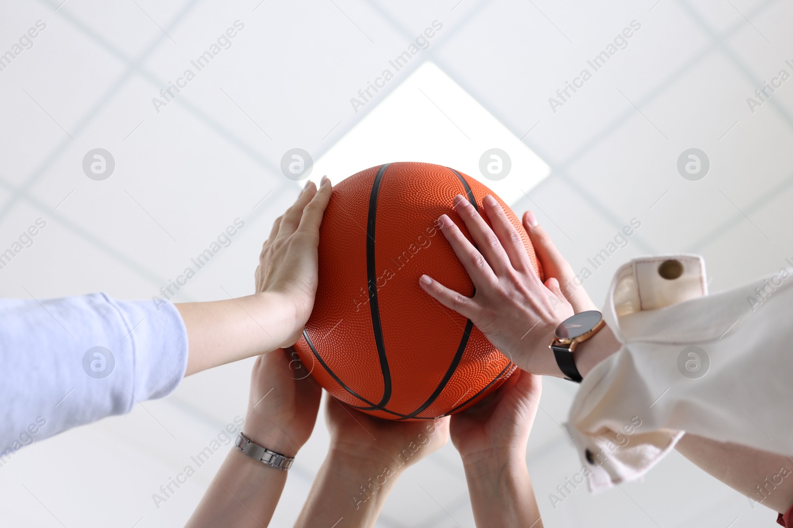 Photo of Unity concept. People holding basketball ball together indoors, low angle view