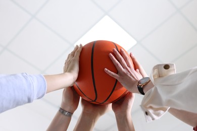 Photo of Unity concept. People holding basketball ball together indoors, low angle view