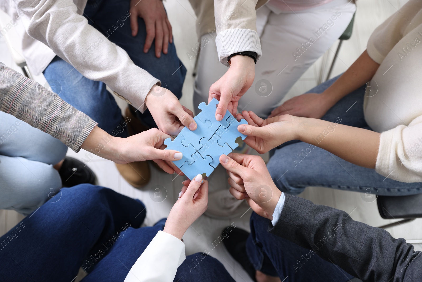 Photo of Unity concept. People putting puzzle pieces together indoors, top view