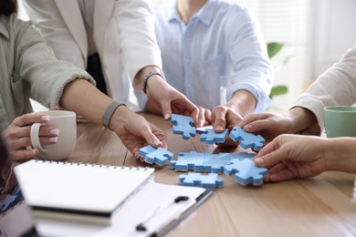 Photo of Unity concept. People putting puzzle pieces together at wooden table indoors, closeup