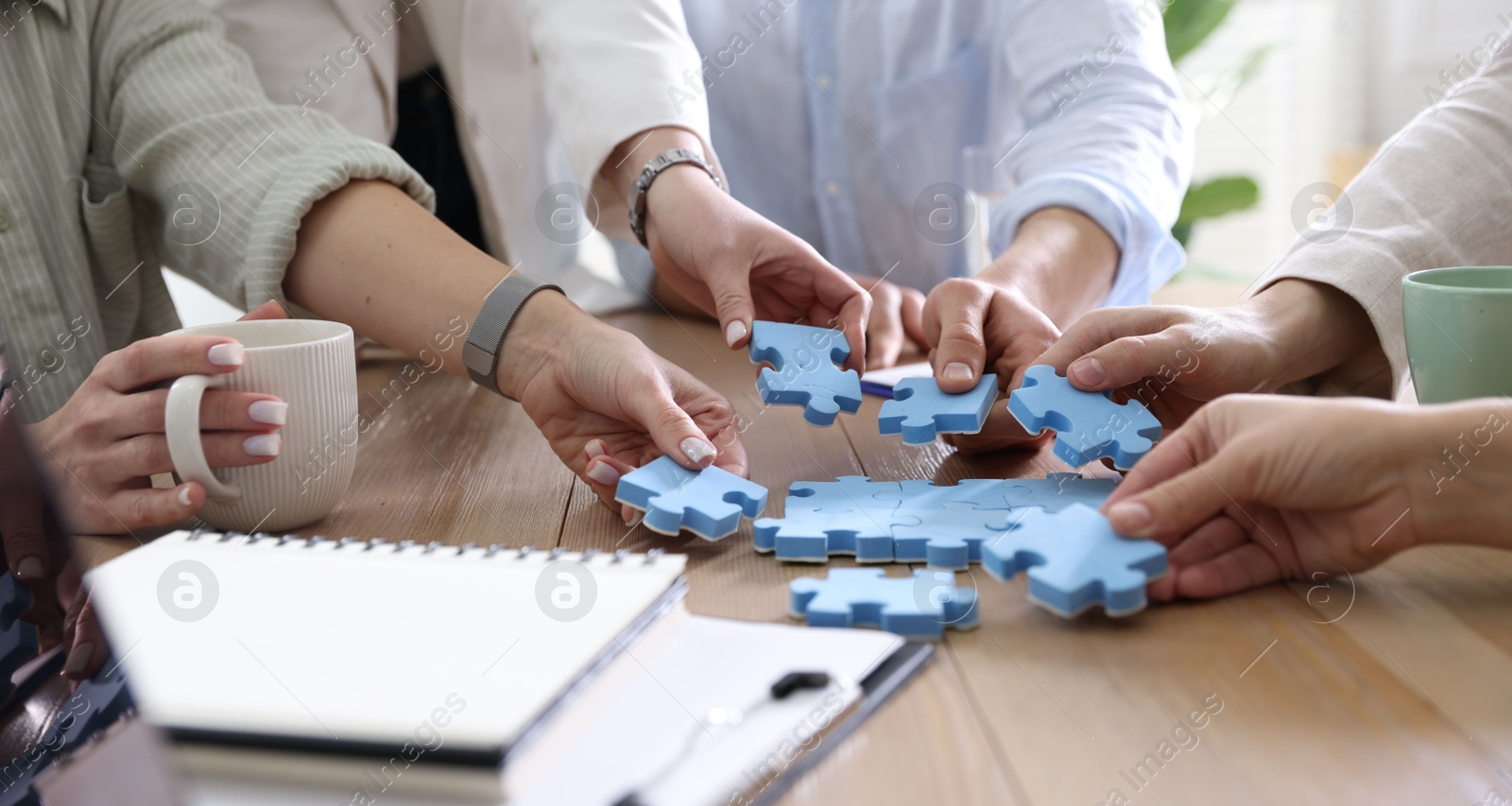 Photo of Unity concept. People putting puzzle pieces together at wooden table indoors, closeup