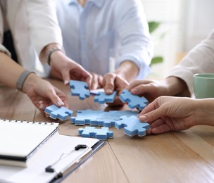 Photo of Unity concept. People putting puzzle pieces together at wooden table indoors, closeup