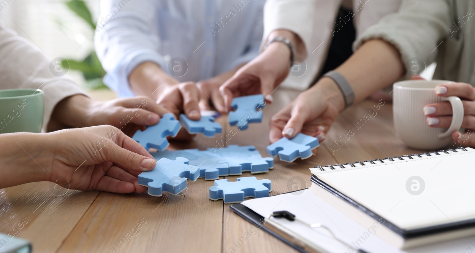 Photo of Unity concept. People putting puzzle pieces together at wooden table indoors, closeup