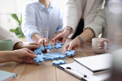 Photo of Unity concept. People putting puzzle pieces together at wooden table indoors, closeup