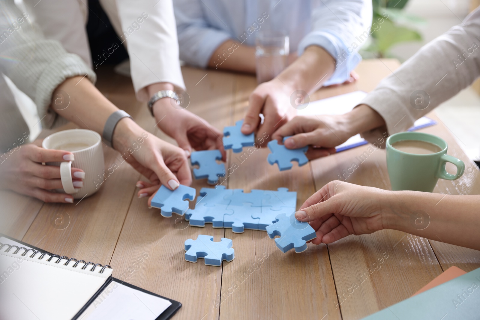 Photo of Unity concept. People putting puzzle pieces together at wooden table indoors, closeup