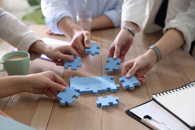 Photo of Unity concept. People putting puzzle pieces together at wooden table indoors, closeup