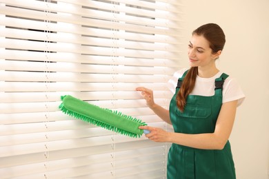 Photo of Professional janitor cleaning dust off window blinds indoors