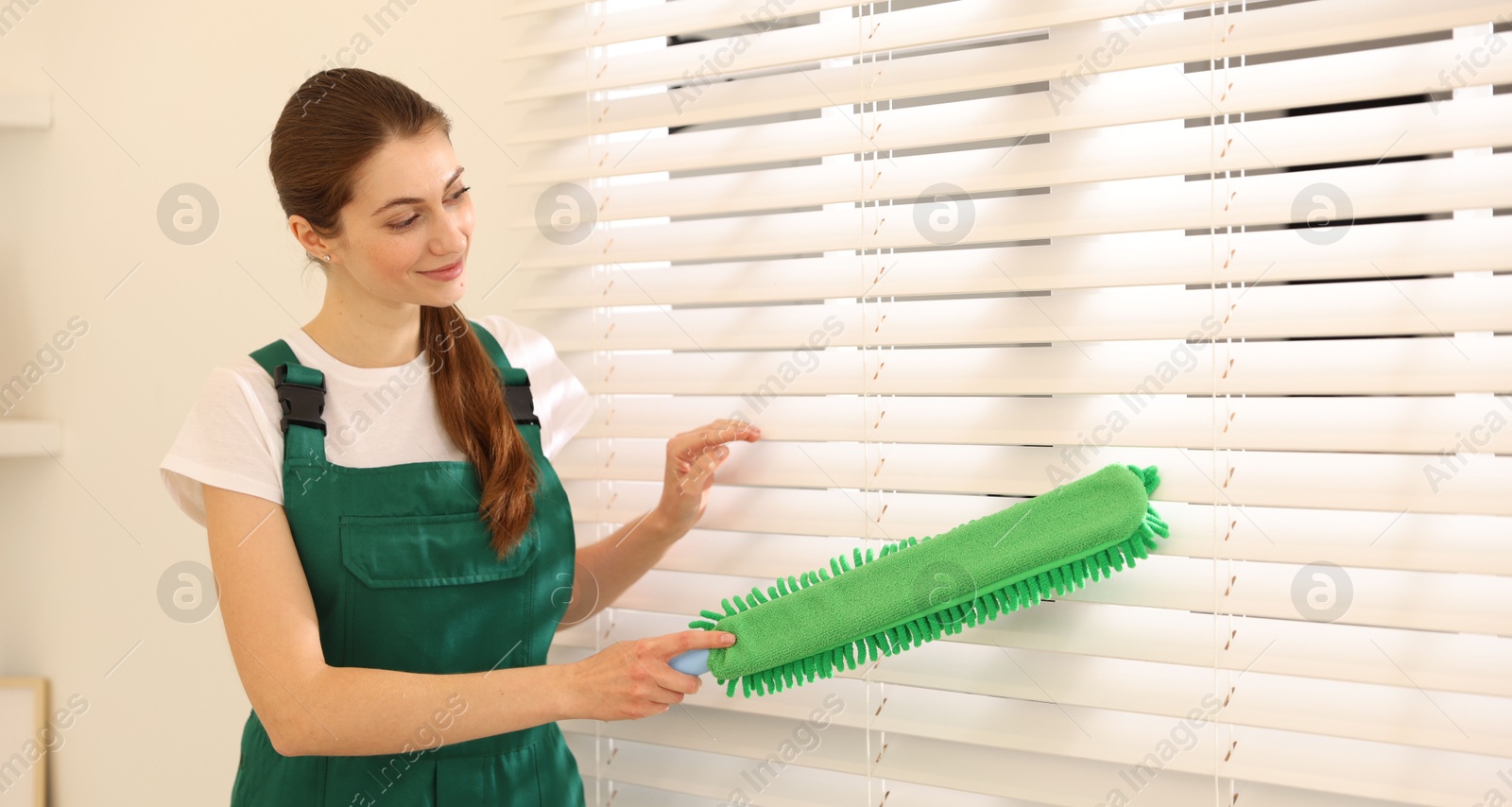 Photo of Professional janitor cleaning dust off window blinds indoors