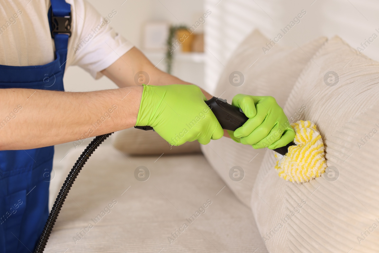 Photo of Professional janitor cleaning sofa with vapor steam system at home, closeup