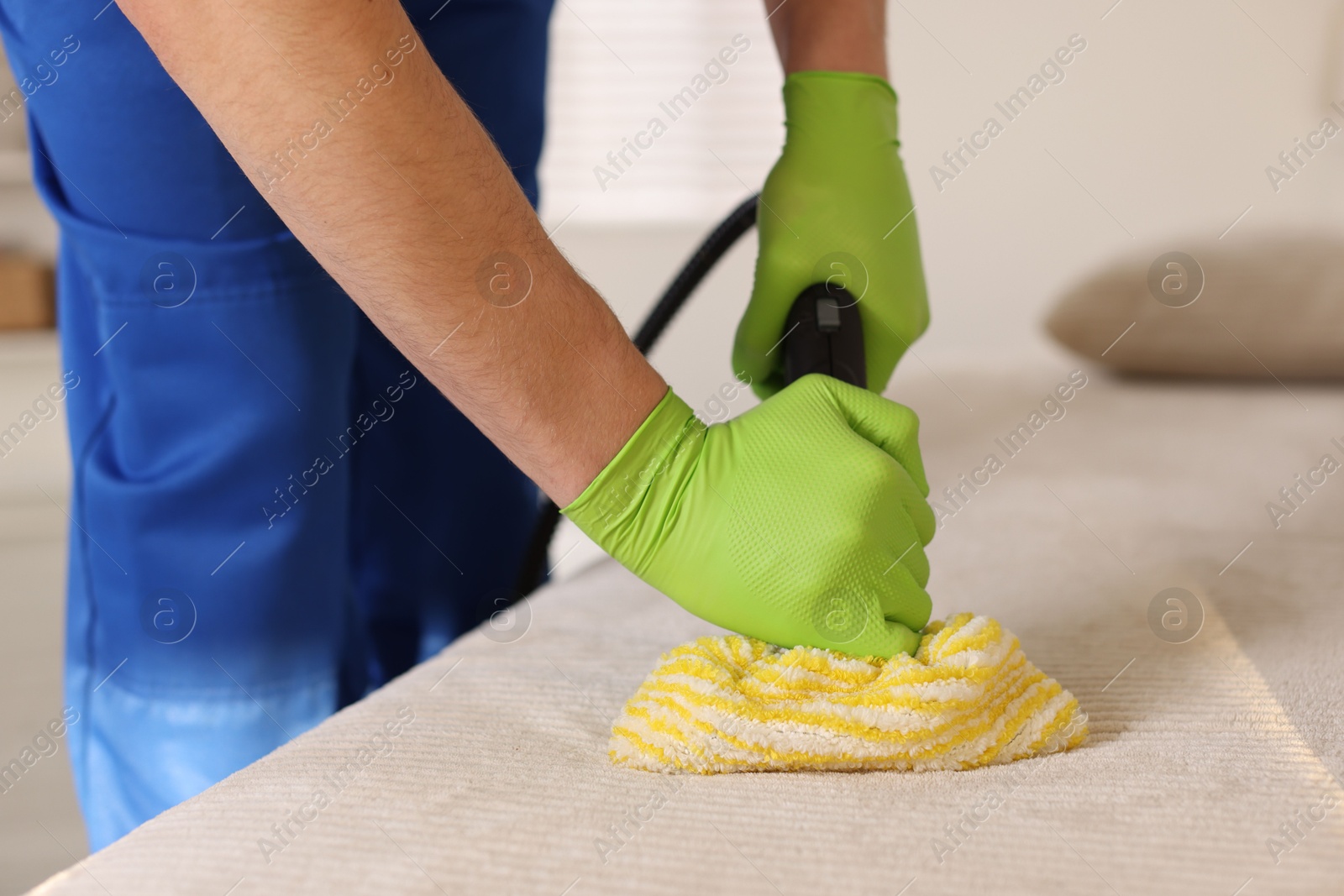 Photo of Professional janitor cleaning sofa with vapor steam system at home, closeup