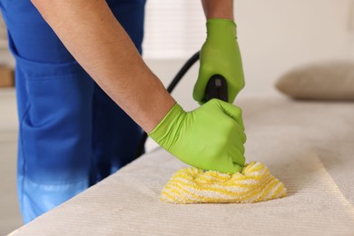 Professional janitor cleaning sofa with vapor steam system at home, closeup